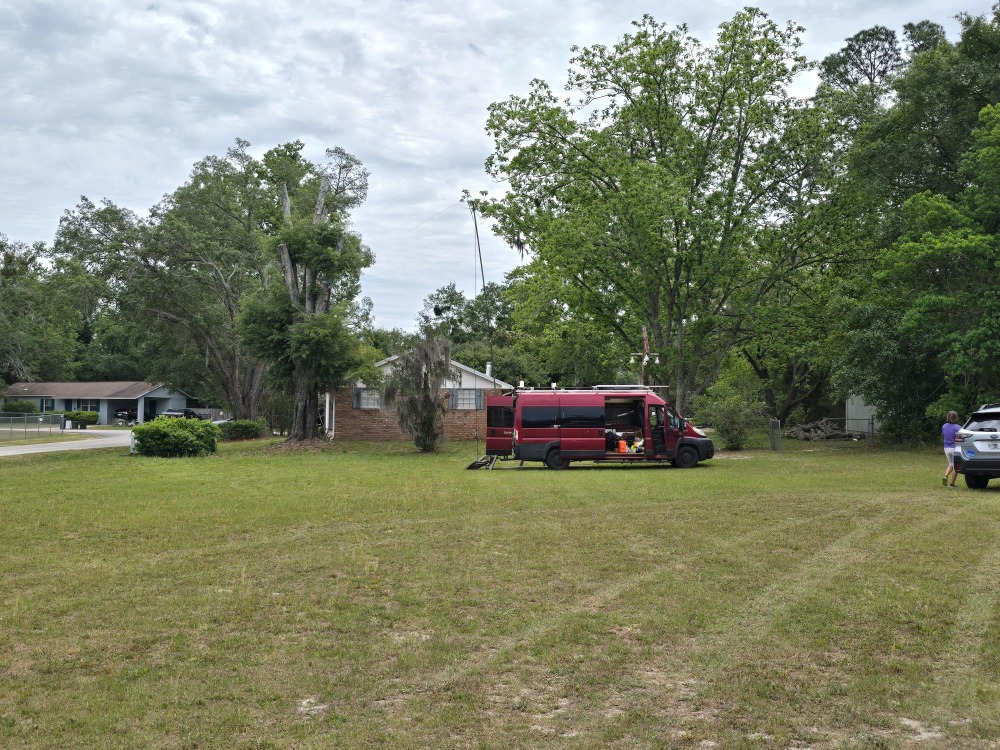 Big Red, a red van, set up as a portable station in a grassy lot with a mast raised from its rear bumper